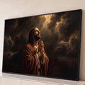 Jesus Cristo de manto marrom orando de mãos unidas sob raios de luz entre nuvens escuras, quadro decorativo