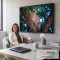 Leopardo com olhar fixo entre troncos de árvore, com folhagem e luz azul desfocada, quadro decorativo