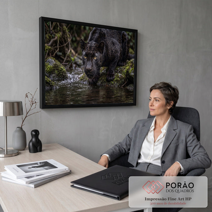 Pantera negra de olhos amarelos agachada à beira de riacho entre pedras com musgo, quadro decorativo
