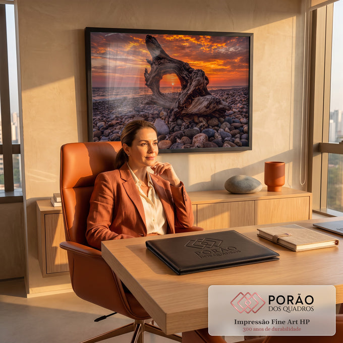 Tronco de madeira emoldurando o pôr do sol laranja sobre o mar em praia de seixos, quadro decorativo
