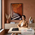 Corredor de arcos terracota com faixas de luz e sombra e pessoa caminhando ao fundo, quadro decorativo