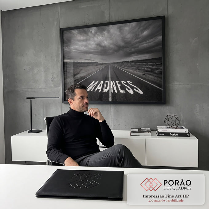Estrada deserta com a palavra Madness pintada no asfalto sob céu nublado em preto e branco, quadro decorativo