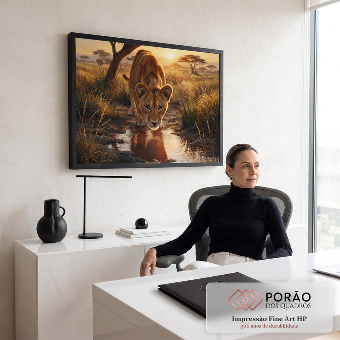 Filhote de leão bebendo água em poça com reflexo, savana dourada e pôr do sol ao fundo, quadro decorativo
