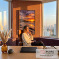Farol branco sobre rochas, praia com pegadas e algas e pôr do sol laranja no mar, quadro decorativo