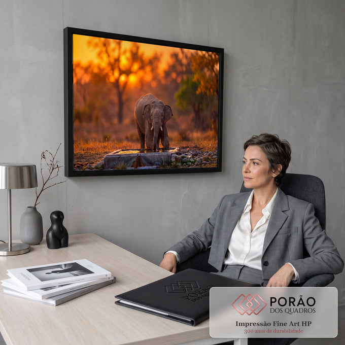 Elefante filhote bebendo água em bebedouro de pedra na savana ao pôr do sol laranja, quadro decorativo
