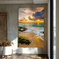Praia ao pôr do sol com ondas, rochas cobertas de musgo e céu dourado com nuvens, quadro decorativo