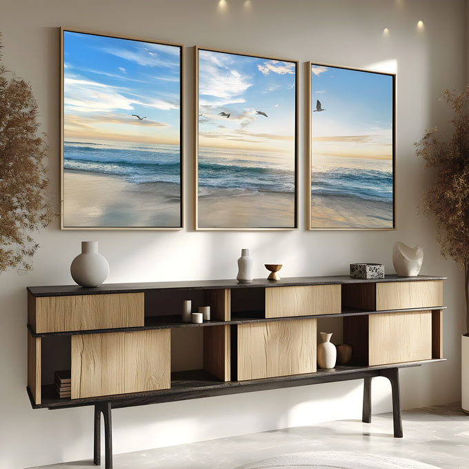 Praia com ondas, gaivotas voando e céu azul com sol baixo no horizonte, quadro decorativo