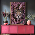 Rosto de onça pintada com olhos azuis cercado por flores rosas e folhas verdes, quadro decorativo