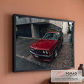 BMW coupé clássico vermelho estacionado em rua molhada com prédios cinza ao fundo, quadro decorativo