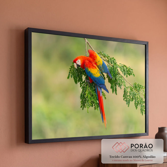 Arara vermelha de asas amarelas e azuis pousada em galho com folhas verdes e fundo desfocado, quadro decorativo
