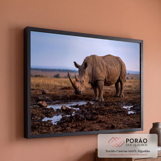 Rinoceronte de chifre longo coberto de lama junto a uma poça na savana africana ao entardecer, quadro decorativo