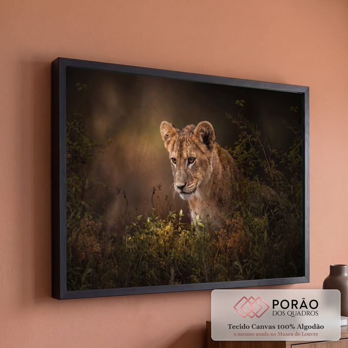 Filhote de leão de olhar atento entre folhagens verdes em fundo escuro e dourado, quadro decorativo