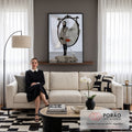 Mulher de casaco geométrico diante de espelho com rosto gigante e garça sobre rochas, quadro decorativo