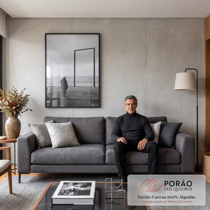 Senhor de casaco escuro olha o mar ao lado de moldura vazia na praia em preto e branco, quadro decorativo