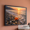 Estrela-do-mar laranja sobre seixos na beira do mar com ondas e pôr do sol dourado ao fundo, quadro decorativo