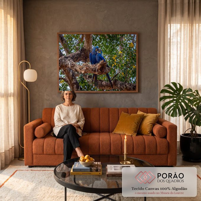 Casal de araras-azuis abraçadas em galho de árvore entre folhagem verde e flores amarelas, quadro decorativo